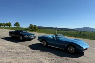 Zwei Autos mit offenem Verdeck vor Berglandschaft und blauem Himmel